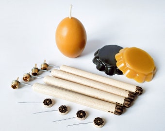 Peut inclure: Un ensemble de cinq outils en bois avec des embouts en laiton pour décorer les bougies. Les outils sont disposés en éventail, les embouts étant tournés vers le spectateur. Il y a également trois petites pièces de cire décoratives rondes dans l'image, deux jaunes et une noire.