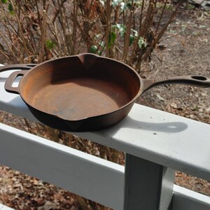 May include: A rusty cast iron skillet with a single handle. The skillet is sitting on a white wooden railing.