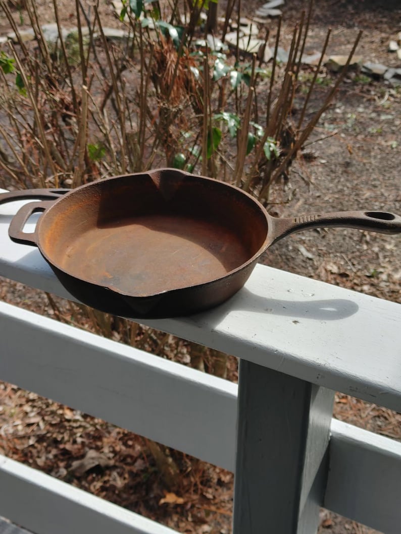 May include: A rusty cast iron skillet with a single handle. The skillet is sitting on a white wooden railing.