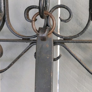 May include: A black metal hook with a decorative scroll design and a ring attached to the top. The hook is mounted on a white wooden surface.