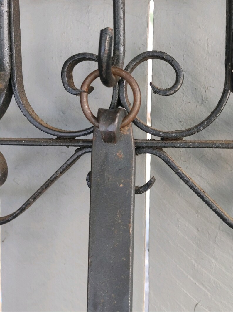 May include: A black metal hook with a decorative scroll design and a ring attached to the top. The hook is mounted on a white wooden surface.