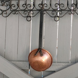 May include: A hammered copper ladle with a black leather handle hanging from a wrought iron rack.