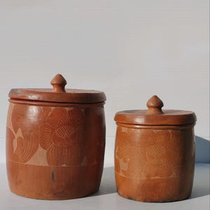 May include: Two brown wooden storage containers with lids. The containers have a carved floral design and are made of wood.