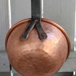 May include: A copper ladle with a hammered finish and a black metal handle. The handle is attached to the ladle with three rivets.
