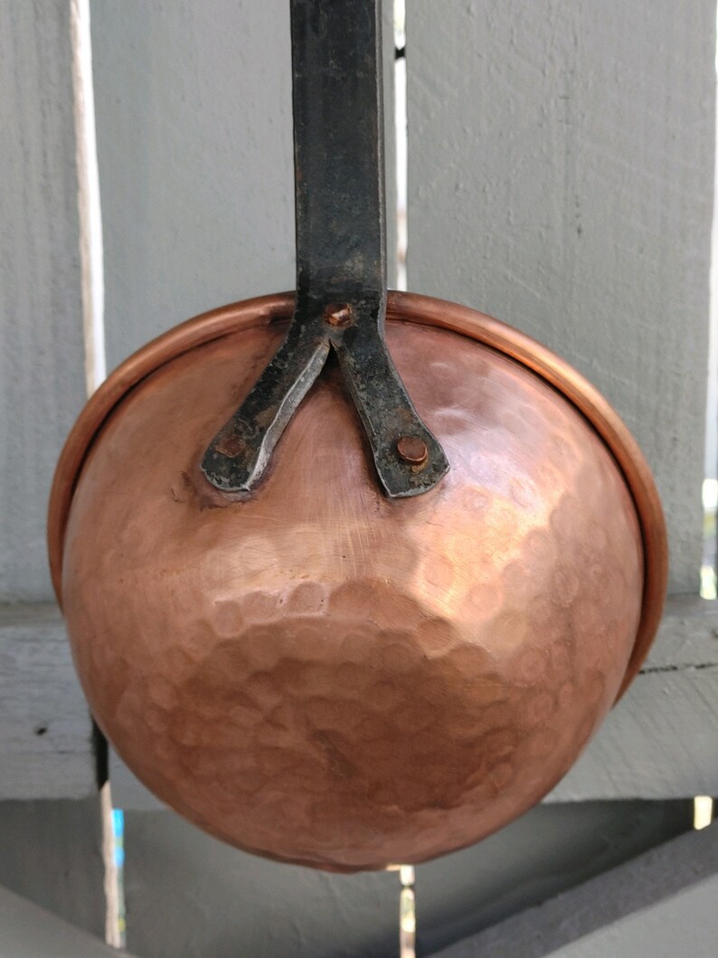 May include: A copper ladle with a hammered finish and a black metal handle. The handle is attached to the ladle with three rivets.