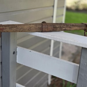 May include: A weathered wooden yoke with metal rings and bands, possibly for an animal. The yoke is a warm brown colour with visible wood grain and signs of age. It rests on a white and grey painted wooden structure.