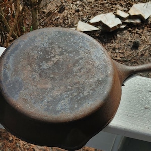 May include: A vintage cast iron skillet with a worn, dark brown patina. The skillet has a single handle and a round cooking surface.