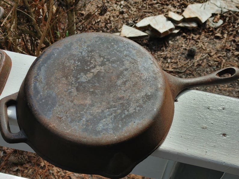 May include: A vintage cast iron skillet with a worn, dark brown patina. The skillet has a single handle and a round cooking surface.