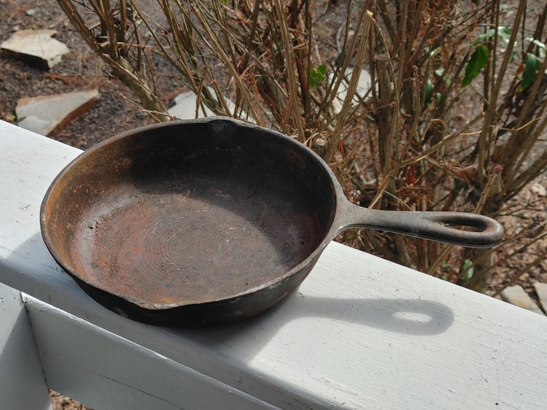 May include: A well-worn cast iron skillet with a dark brown patina. The skillet has a long handle with a loop at the end.