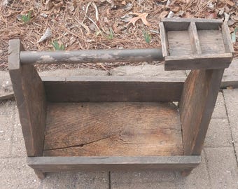 May include: A rustic wooden tool caddy with a handle and a small tray on top. The caddy is made of weathered wood and has a natural brown colour.