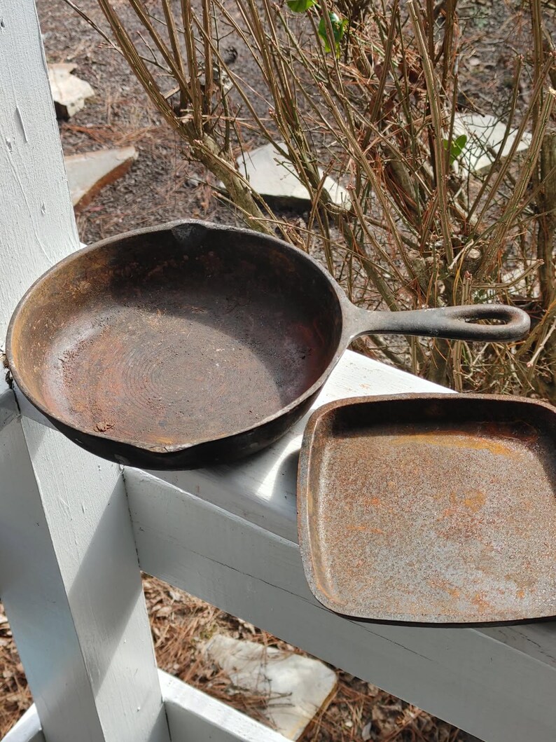 May include: Two cast iron skillets, one round and one square, both with a rusty brown patina.