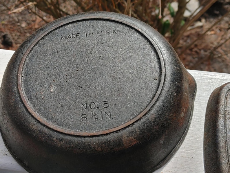 May include: A cast iron skillet with a black finish. The bottom of the skillet is marked "MADE IN USA" and "NO. 5 8 1/2 IN."