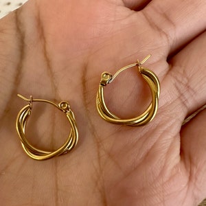 May include: A pair of gold-toned hoop earrings with a twisted design. The earrings are small and delicate.