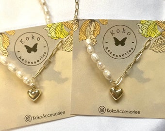 May include: Two gold necklaces with a heart charm and pearl accents. The necklaces are displayed on a card with the text "Koko Accessories" and a butterfly logo.