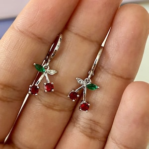 Peut inclure: Une paire de boucles d'oreilles pendantes en argent avec des cerises en cristal rouge et vert. Les boucles d'oreilles ont un design en forme de cercle et sont parfaites pour ajouter une touche de fantaisie à n'importe quelle tenue.