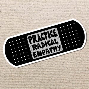 May include: A black and white bandage sticker featuring the words "PRACTICE RADICAL EMPATHY". The text is in a bold, blocky font. The sticker has a white border and small white dots. The background is a textured, beige surface.