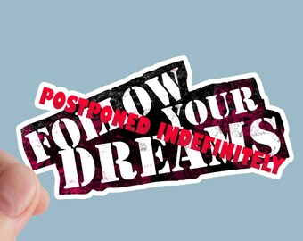 Può includere: Un adesivo con la scritta "FOLLOW YOUR DREAMS" in bianco, con la scritta rossa "POSTPONED INDEFINITELY" sovrapposta. Il design è in stile grunge, con sfondo nero e rosa.