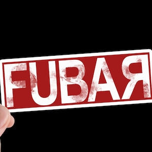 Puede incluir: Una pegatina rectangular con la palabra "FUBAR" en blanco, con fuente desgastada, sobre un fondo rojo. La pegatina está sujeta por una mano sobre un fondo negro.