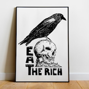 Può includere: Stampa artistica in bianco e nero con un'illustrazione dettagliata di un corvo appollaiato su un teschio umano. Il testo in grassetto sottostante recita "EAT THE RICH". L'opera è incorniciata in nero, creando un forte contrasto.