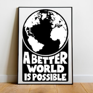 Puede incluir: Impresión enmarcada en blanco y negro con una ilustración estilizada del globo terráqueo. El texto "A Better World Is Possible" está escrito en letras blancas debajo. La obra de arte está sobre un fondo blanco.