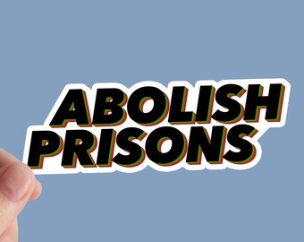 May include: A sticker with the words "ABOLISH PRISONS" in bold black letters with red and green outlines. The sticker is held by a hand against a light blue background.