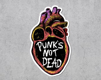 May include: A sticker depicting an anatomical heart in shades of red, yellow, and purple. The text "PUNK'S NOT DEAD" is written in white on a black area within the heart. The sticker has a white border and is set against a grey background.