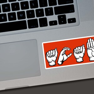 May include: A rectangular sticker with the word "HOPE" spelled out in American Sign Language, featuring white hand illustrations on a bright orange background. The sticker is placed on a laptop.
