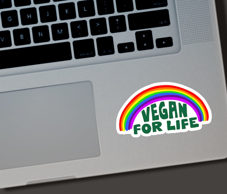 May include: A white sticker with a rainbow arc and the words "VEGAN FOR LIFE" in green. The sticker is on a laptop. The rainbow has red, orange, yellow, green, blue, and purple colors.