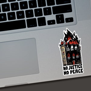 Puede incluir: Una pegatina con un edificio en llamas en rojo y negro. La pegatina tiene el texto "NO JUSTICE NO PEACE" en blanco. La pegatina est&aacute; colocada en un port&aacute;til plateado.
