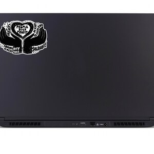 May include: Black laptop with a sticker featuring a heart-shaped design held by two hands. The sticker includes the text "People Over Profit," "Solidarity," "Community is Resistance," and "Help Others, Be Kind to Every Kind."