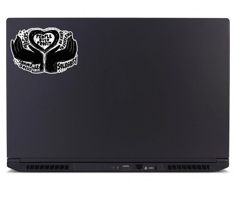 May include: Black laptop with a sticker featuring a heart-shaped design held by two hands. The sticker includes the text "People Over Profit," "Solidarity," "Community is Resistance," and "Help Others, Be Kind to Every Kind."