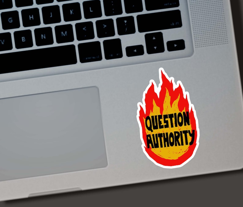 May include: A sticker with a flame design in red and yellow, with the words "QUESTION AUTHORITY" in black. The sticker is placed on a silver laptop.