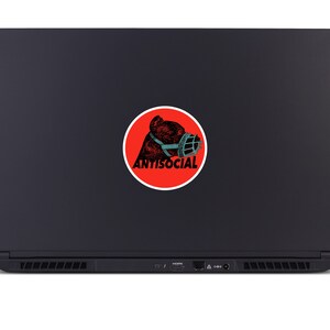May include: A black laptop with a round sticker featuring a bear wearing a muzzle. The sticker has a red background with the word "ANTISOCIAL" in white text. The bear illustration is in shades of brown and teal.