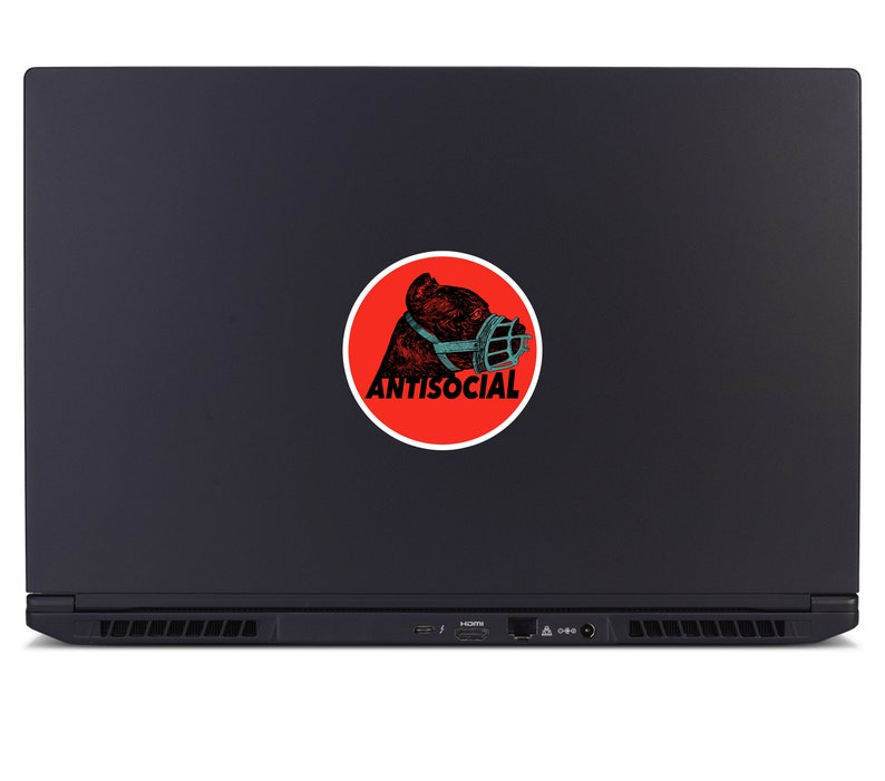 May include: A black laptop with a round sticker featuring a bear wearing a muzzle. The sticker has a red background with the word "ANTISOCIAL" in white text. The bear illustration is in shades of brown and teal.
