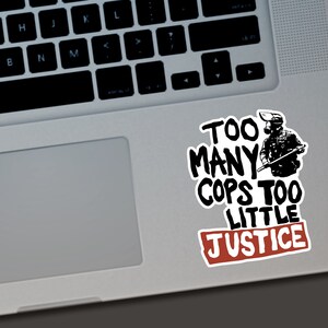 Puede incluir: Una pegatina blanca con texto negro y un rect&aacute;ngulo rojo. El texto dice "TOO MANY COPS TOO LITTLE JUSTICE" con una ilustraci&oacute;n de una persona con equipo t&aacute;ctico. La pegatina est&aacute; en un port&aacute;til.