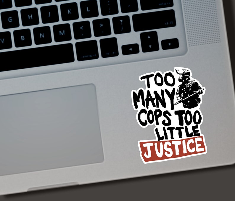 Puede incluir: Una pegatina blanca con texto negro y un rect&aacute;ngulo rojo. El texto dice "TOO MANY COPS TOO LITTLE JUSTICE" con una ilustraci&oacute;n de una persona con equipo t&aacute;ctico. La pegatina est&aacute; en un port&aacute;til.