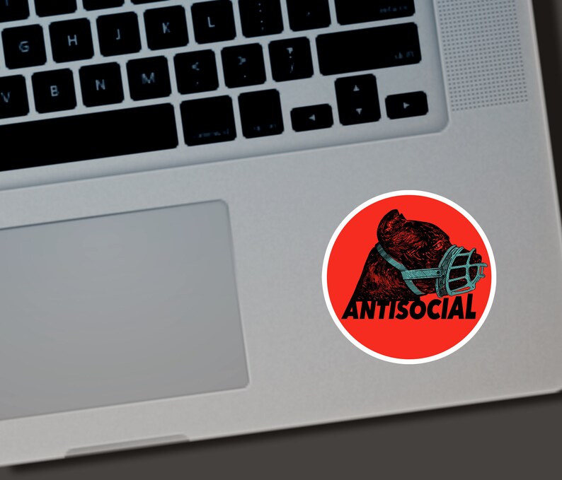 May include: A round sticker with a red background featuring a black and teal illustration of a dog wearing a muzzle. The word "ANTISOCIAL" is printed in white below the dog illustration.