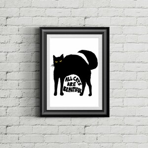 May include: Black framed art print featuring a black cat silhouette with yellow eyes. The text "ALL CATS ARE BEAUTIFUL" is printed in white within the cat's body. The artwork is displayed against a white background and a brick wall.