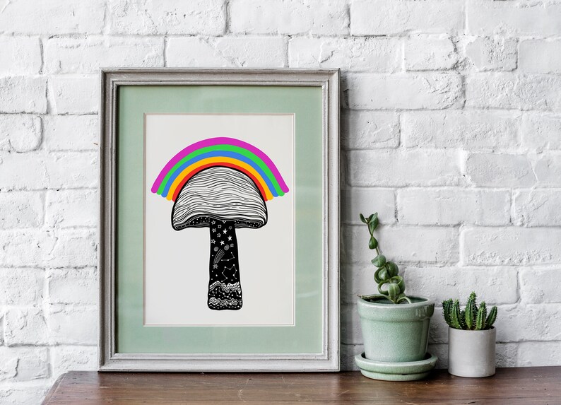 May include: A framed art print featuring a whimsical mushroom design with a rainbow arching over the cap. The mushroom has a black and white patterned cap and stem, with stars and other details. The frame is a light green color.