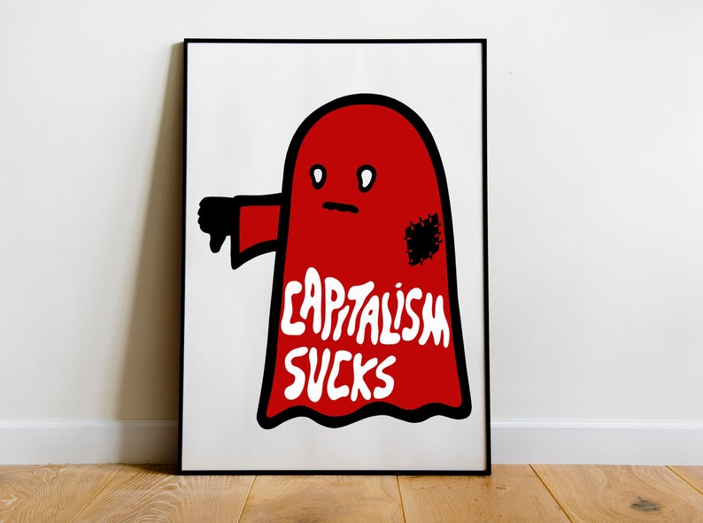May include: A framed art print featuring a red ghost-like figure with a black thumb down and the words "CAPITALISM SUCKS" in white. The artwork has a minimalist design and is set against a white background.