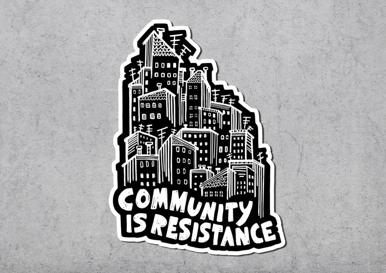 May include: A black and white sticker featuring a stylized cityscape with the text "COMMUNITY IS RESISTANCE" in bold, white letters. The illustration depicts buildings with antennas and various architectural details, creating a graphic design.