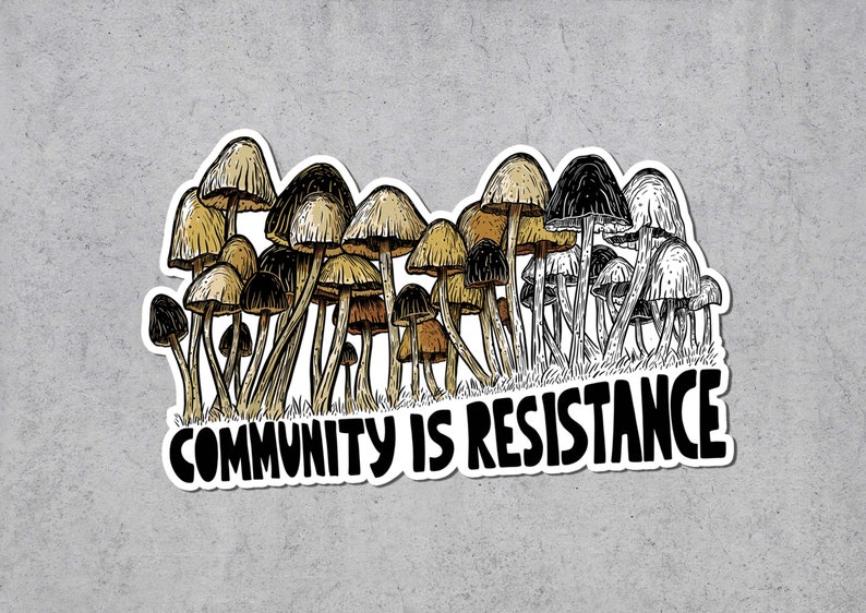 May include: A sticker featuring a cluster of stylized mushrooms in shades of brown, tan, and black. The text "COMMUNITY IS RESISTANCE" is written in bold, black letters below the mushrooms. The sticker has a white border.