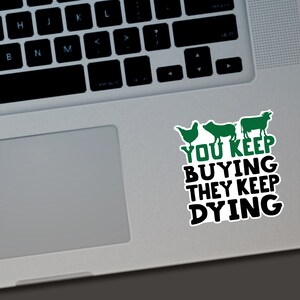 May include: A white sticker with a green chicken, pig, and cow illustration, and the text "YOU KEEP BUYING THEY KEEP DYING" in black and green. The sticker is on a laptop.