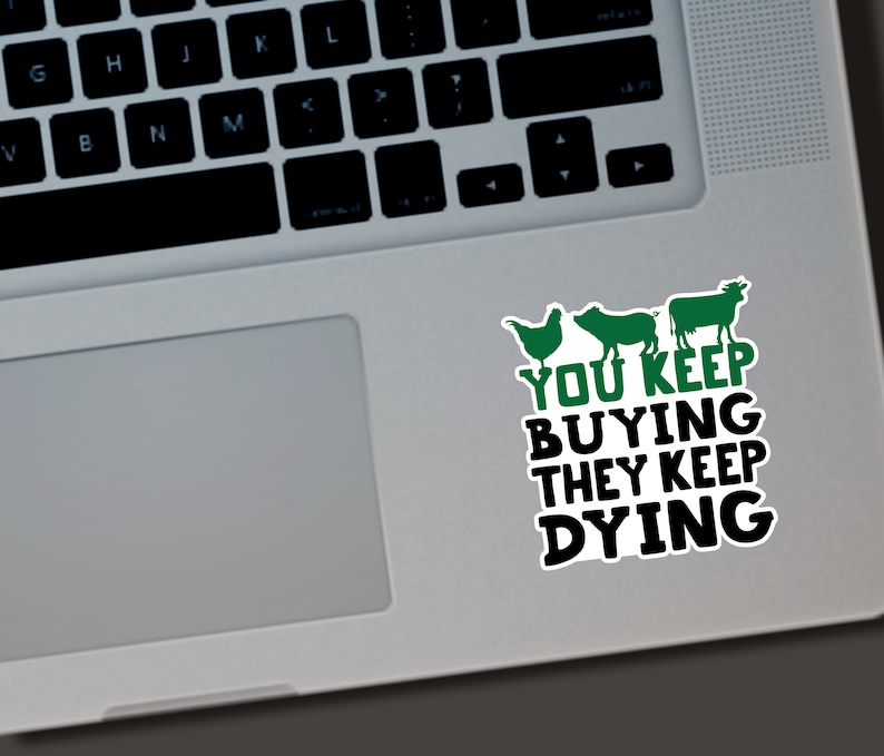 May include: A white sticker with a green chicken, pig, and cow illustration, and the text "YOU KEEP BUYING THEY KEEP DYING" in black and green. The sticker is on a laptop.