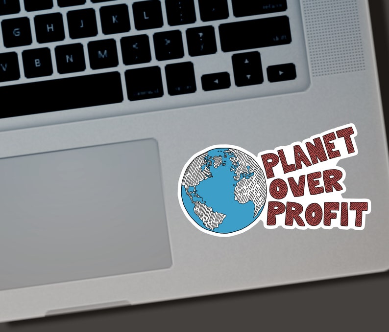 Puede incluir: Una pegatina blanca con una ilustraci&oacute;n de un globo terr&aacute;queo azul y blanco y el texto rojo "PLANET OVER PROFIT". La pegatina est&aacute; colocada en un port&aacute;til plateado.