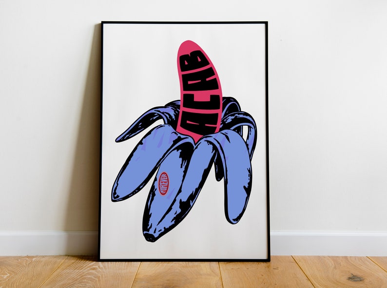 May include: Pop art style print featuring a peeled banana with a pink fruit and blue peel. The word "ACAB" is printed in black on the pink fruit. The print is framed in a black frame and set against a white background.