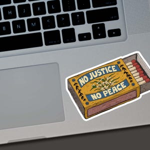 May include: A sticker of a matchbox with the words "NO JUSTICE NO PEACE" in blue on a yellow background. The matchbox contains several matches with red tips. The sticker is on a laptop.