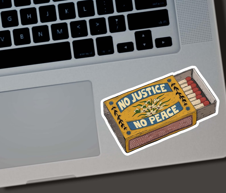 May include: A sticker of a matchbox with the words "NO JUSTICE NO PEACE" in blue on a yellow background. The matchbox contains several matches with red tips. The sticker is on a laptop.