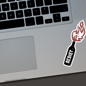 May include: A sticker featuring a stylized illustration of a Molotov cocktail. The bottle is black with the word "RESIST" in white lettering. The flames are red and white, suggesting a protest or resistance theme.