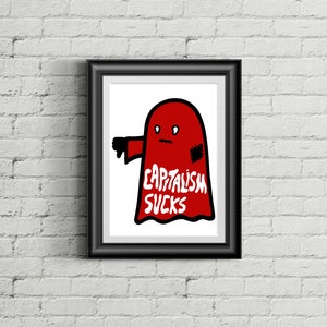 May include: Framed art print featuring a red ghost with a thumbs-down gesture. The ghost has the words "CAPITALISM SUCKS" in white text. The artwork is displayed in a black frame against a white brick wall.